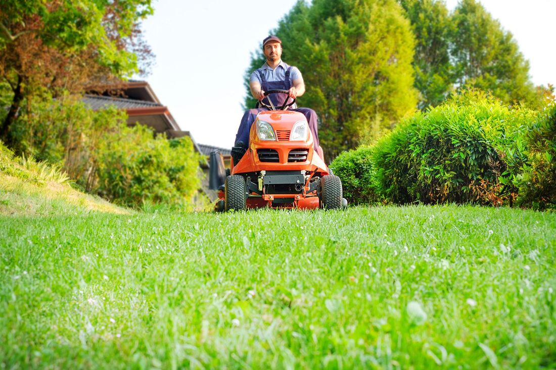 Gardener sitting on a riding lawn mower, mowing an acreage